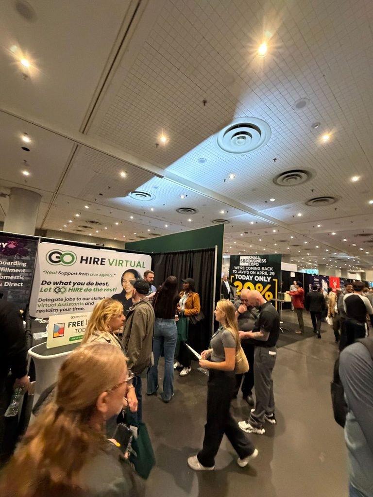 go-hire-virtual-networking-small-business-expo-new-york | Go Hire Virtual - Virtual Assistants for just Crowd at a job fair or expo with booths; prominent GO HIRE VIRTUAL banner in the foreground and attendees talking nearby.